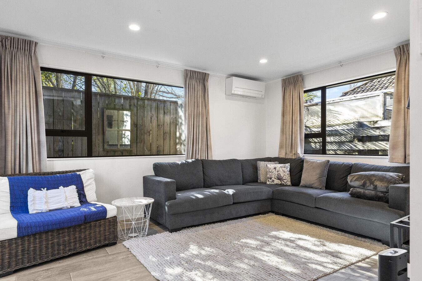A modern living room with a grey sectional sofa, a wicker sofa, and a small round table.
