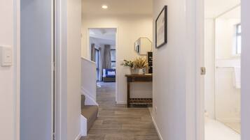 A hallway with a wooden floor, a staircase, a wall-mounted lamp, and a welcome sign.
