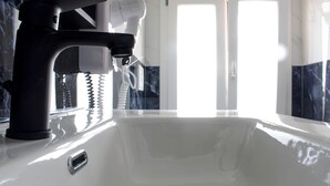 A modern bathroom with a white sink, a black faucet, and a hairdryer mounted on the wall.
