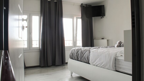 A bedroom with a bed, a TV mounted on the wall, and a window with curtains.