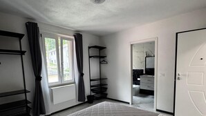 A hotel room with a large bed, a wardrobe, a bathroom with a mirror, and a window with curtains.