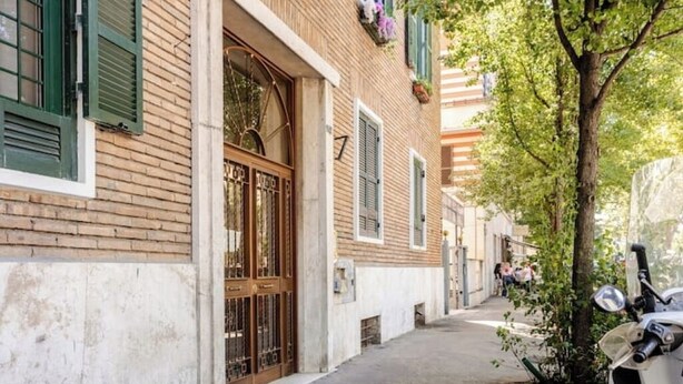 A narrow street with a brick building, a wooden door, and a tree. - Vatican Area | Stylish 2BR + Fast Wi-Fi & A/C (Roma)