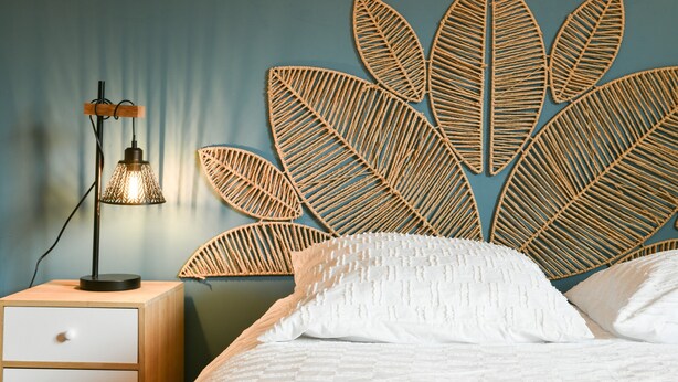 A bed with white bedding, a bedside lamp, and a wall-mounted leaf-patterned decor.