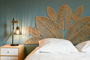 Una cama con ropa blanca, una lámpara de noche y decoración con motivos de hojas en la pared.