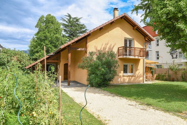 Une maison à deux étages avec un balcon, un jardin et une allée gravillonnée.