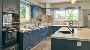 A modern kitchen with dark blue cabinets, a built-in oven, a large island with a sink, and a window with a view of greenery.