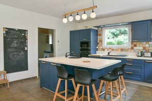 Une cuisine moderne dotée d’un grand îlot central, de tabourets de bar et d’un tableau noir sur lequel on peut écrire.