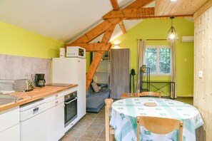 Une cuisine compacte équipée d’un four à micro-ondes, d’une machine à café et d’un comptoir en bois. On y trouve un coin repas avec une table et des chaises, ainsi qu’un petit coin salon avec un canapé.