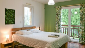 A bedroom with a bed, bedside table, lamp, window, and a view of a balcony.