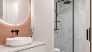 A modern bathroom with a white sink, a round mirror with a wooden frame, and a glass-enclosed shower with a marble wall. - The Vietta Hotel | Double Double | Near Disney’s Wonders (Kissimmee)
