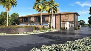 Un hotel moderno con techo plano, palmeras y un jardín cuidado.
