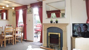 A cozy living room with a fireplace, a dining area with wooden chairs, and a television. - Mobile Home in Kolczewo With a Terrace (gmina Wolin)