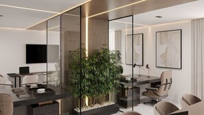 A modern office space with glass partitions, a large plant, and a laptop on a desk.