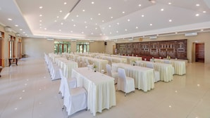 A large banquet hall with multiple tables and chairs, high ceiling with recessed lighting, and a decorative wooden panel on the back wall. - Pelangi Hotel at Artotel Pelangi Park (Bogor)