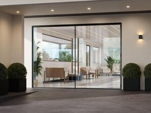 Un hall d’entrée moderne avec une cloison en verre, un espace salon et des plantes en pot.