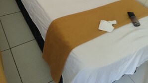 Una cama individual con ropa blanca de cama y una manta marrón, un control remoto y un pañuelo sobre la cama.