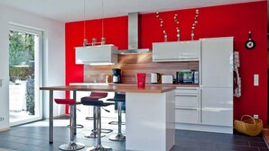 A modern kitchen with a central island, bar stools, and a red accent wall.