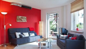A living room with a red wall, two sofas, a coffee table, a lamp, and a window with blinds.