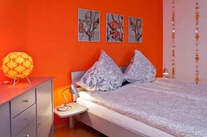 Un dormitorio con cama, almohadas, una mesita de noche, lámpara y decoración en la pared.
