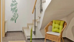 A room with a staircase, a wicker chair with a cushion, and a wall with a bamboo plant decoration.
