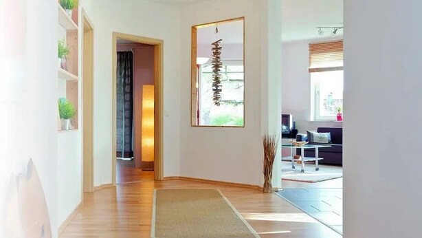 A spacious room with wooden flooring, a large window, and a door leading to another area.
