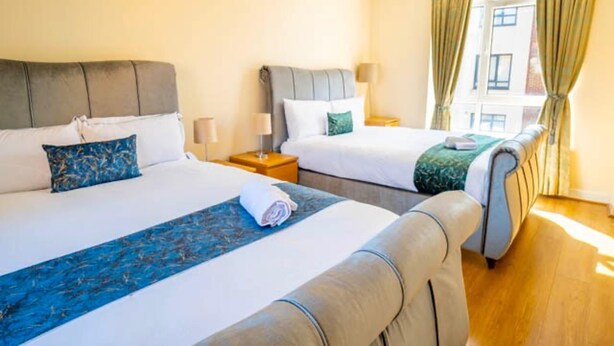 A hotel room with two beds, a wooden floor, and a window with curtains. - 14 Guests-6 Bedroom House, Free Parking (Milton Keynes)