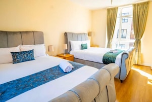 A hotel room with two beds, a wooden floor, and a window with curtains.
