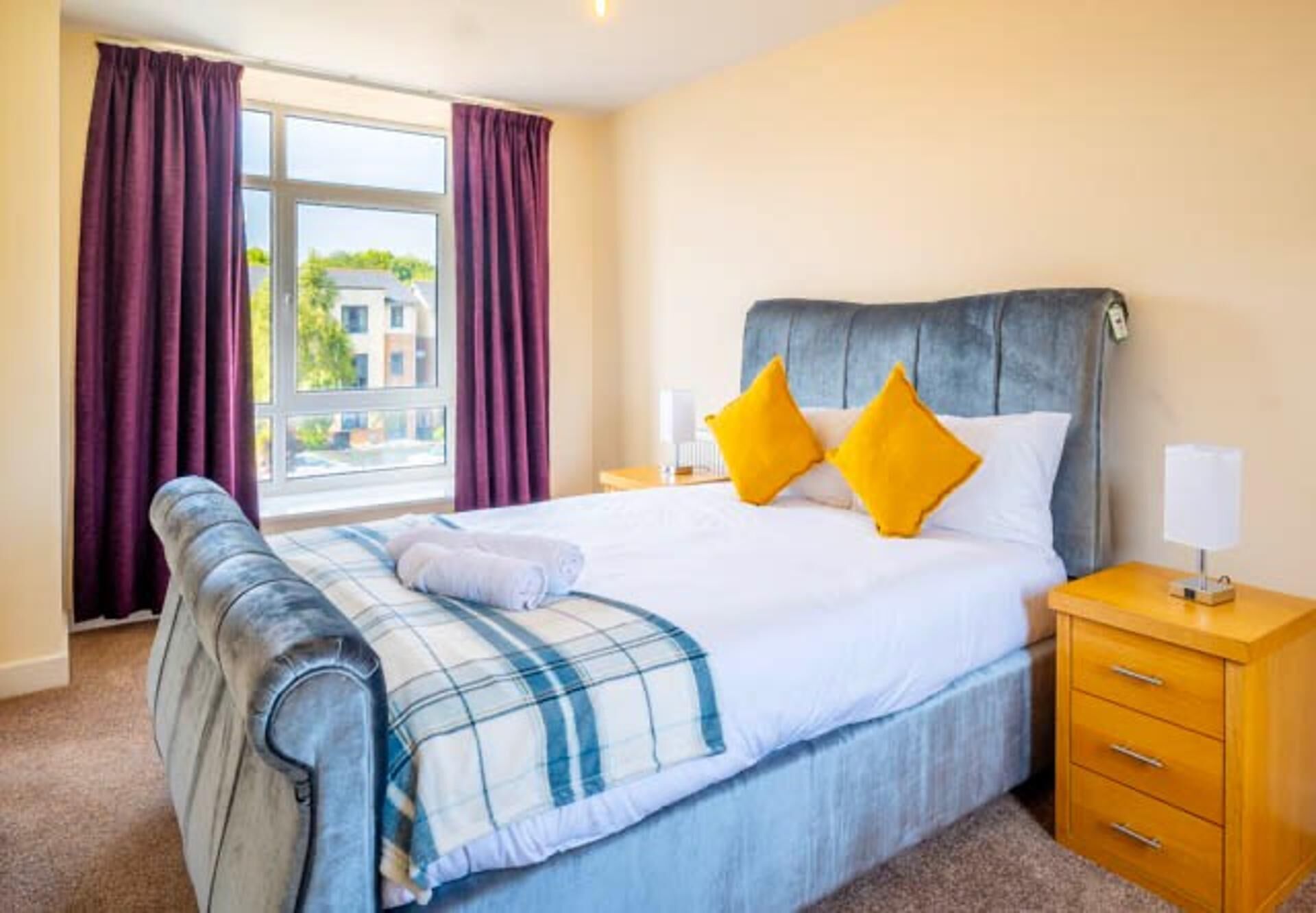A hotel room with a bed, a nightstand, a lamp, and a window with curtains.