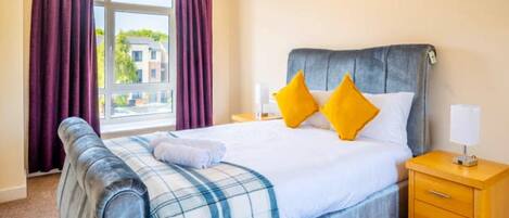 A hotel room with a bed, a nightstand, a lamp, and a window with curtains.