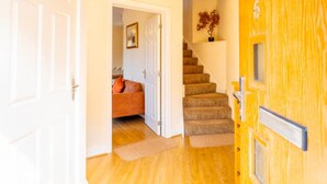 A hallway with a wooden door, a staircase, and a room with a sofa and a plant. - 14 Guests-6 Bedroom House, Free Parking (Milton Keynes)