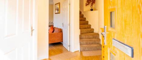 A hallway with a wooden door, a staircase, and a room with a sofa and a plant.