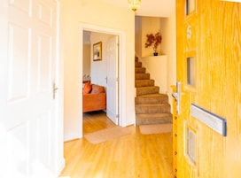 A hallway with a wooden door, a staircase, and a room with a sofa and a plant.