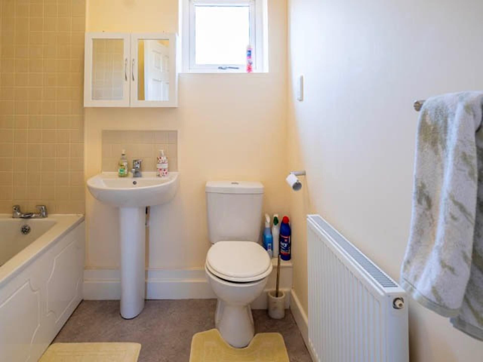 Un bagno piccolo e pulito con lavandino, water e vasca da bagno bianchi. Sul lavandino ci sono articoli da toilette e un asciugamano appeso al muro.