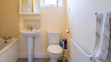 Un bagno piccolo e pulito con lavandino, water e vasca da bagno bianchi. Sul lavandino ci sono articoli da toilette e un asciugamano appeso al muro.