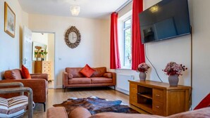 A living room with a sofa, a wooden cabinet, a TV, and a clock on the wall. - 14 Guests-6 Bedroom House, Free Parking (Milton Keynes)
