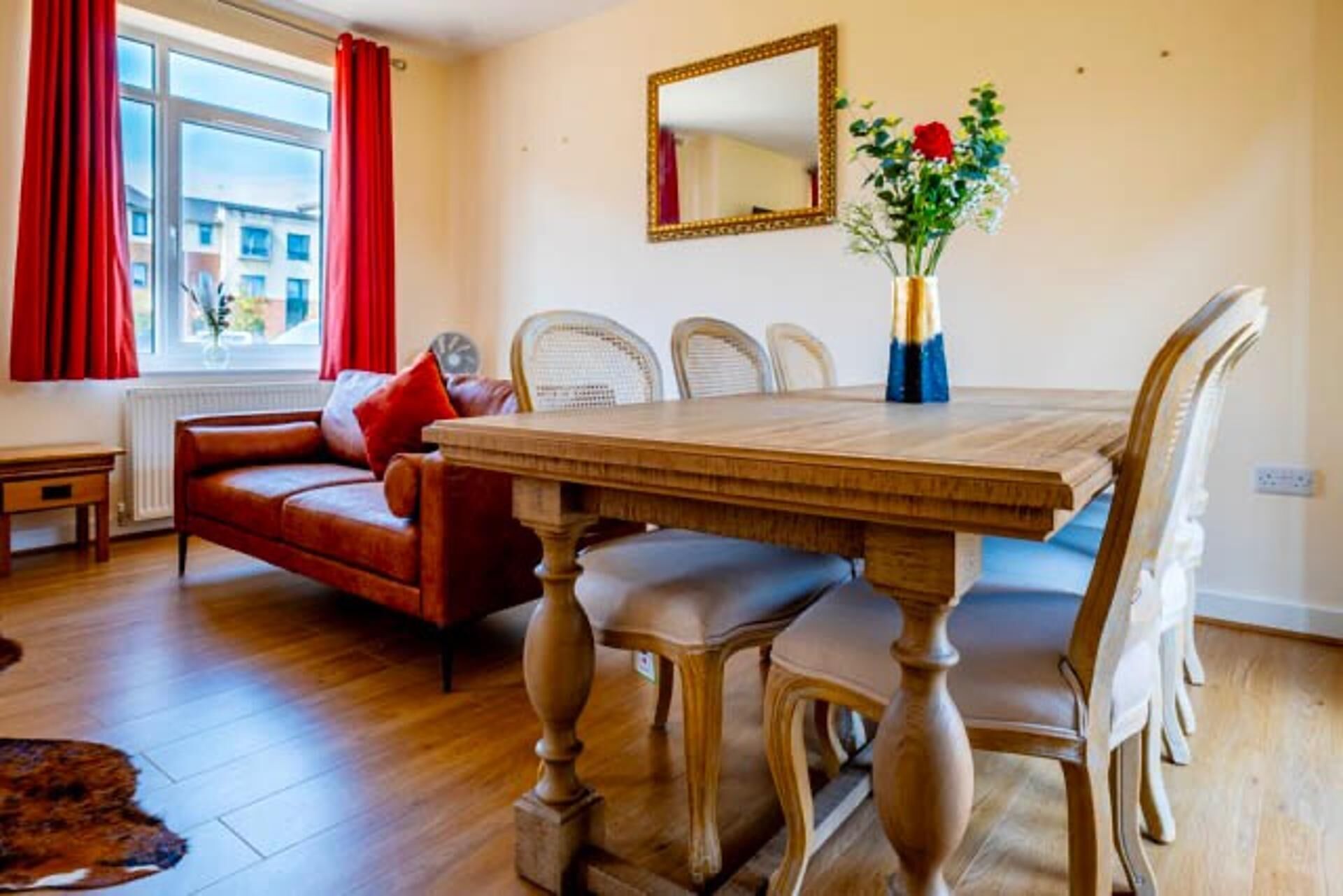 A dining area with a wooden table and chairs, a red sofa, and a mirror on the wall.