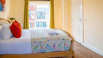 Un dormitorio con cama, ventana con cortinas, puerta y un cuadro en la pared.
