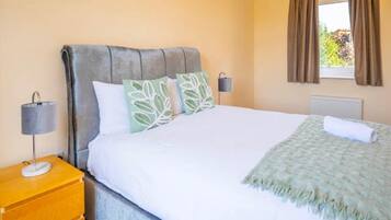 A bedroom with a bed, a nightstand, a lamp, and a window with curtains.