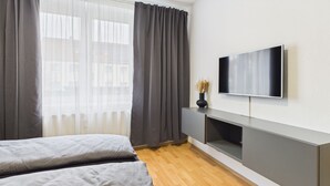A modern bedroom with a bed, a TV mounted on the wall, and a wooden floor.