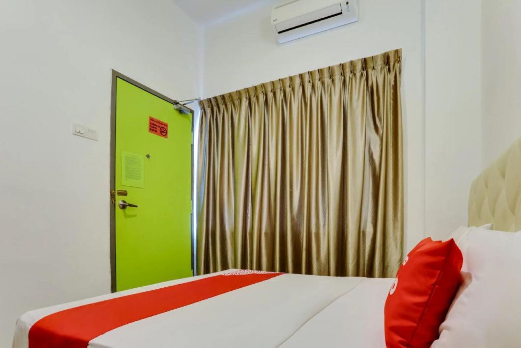Een hotelkamer met een bed, een groene deur en een raam met gordijnen.