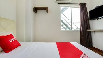 Quarto de hotel com cama, janela com vista para uma escadaria, ar condicionado e televisão na parede.