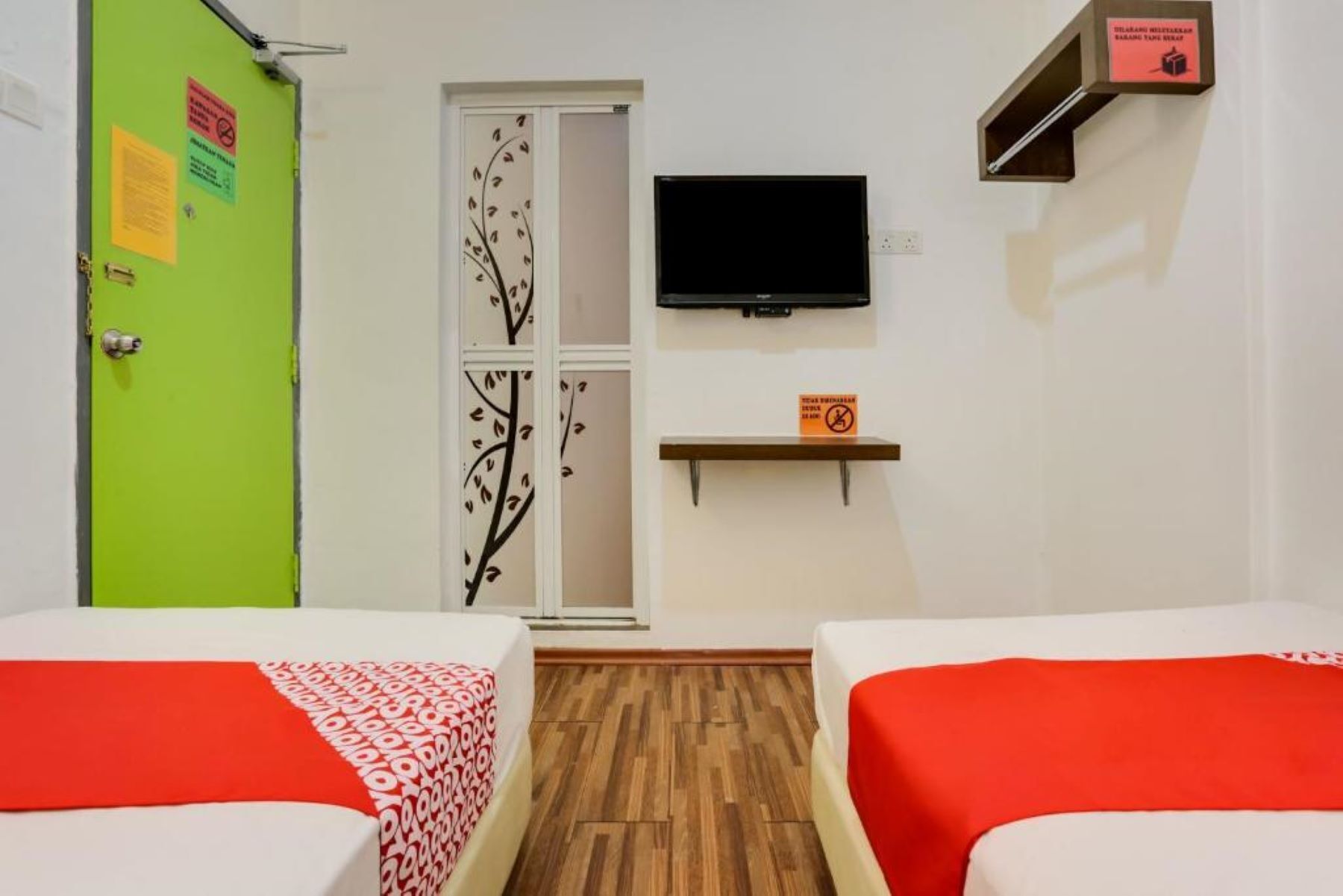 A hotel room with two beds, a television, a shelf, and a door with a tree decal.