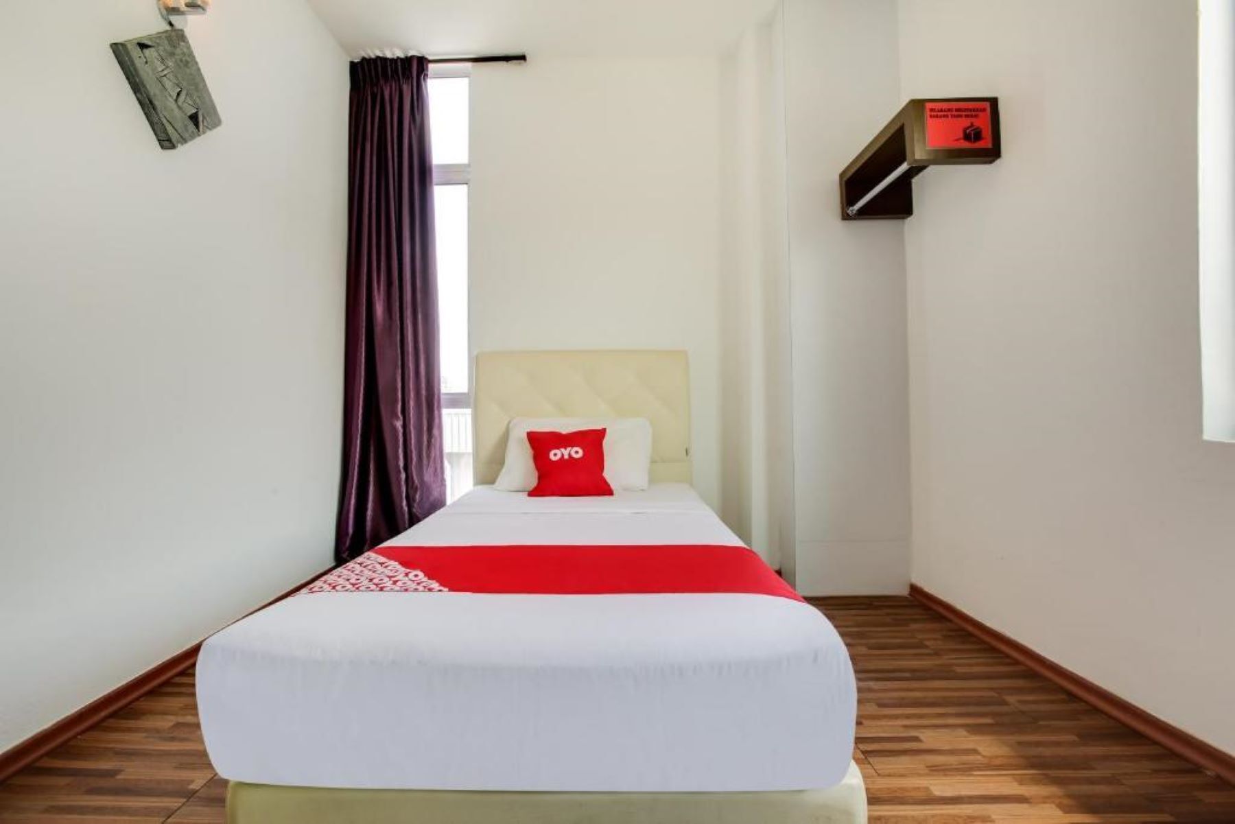 A small, neatly arranged room with a bed, a window with curtains, a wall-mounted shelf, and a wooden floor.