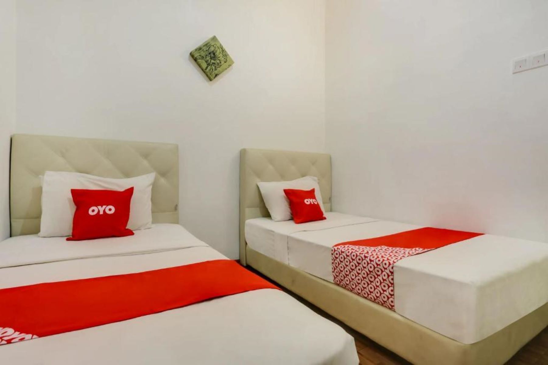 Dos camas individuales con cabeceros, cada una con una almohada roja y una colcha blanca.