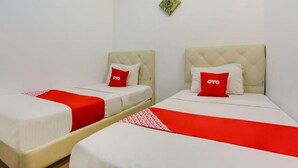 Zwei Doppelbetten mit roter und weißer Bettwäsche, eine grüne, rautenförmige Dekoration an der Wand und ein rot-weiß gemusterter Teppichläufer.