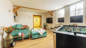 Ein gemütliches Wohnzimmer mit einem grünen Sofa, einem Kicker und einem Holzbalken an der Decke.