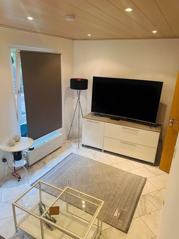 Un salon moderne avec un téléviseur à écran plat, un lampadaire, une table basse en verre et un tapis à motifs.