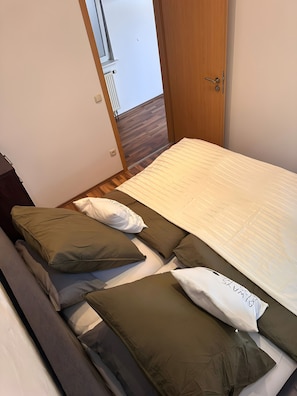 Une chambre à coucher avec un lit, des oreillers, un plancher en bois, une porte et une fenêtre.