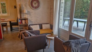Ein Wohnzimmer mit einer Couch, Sesseln, einem kleinen Tisch, einem Bücherregal und einem großen Fenster.