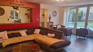 Ein Wohnzimmer mit Ecksofa, Couchtisch, Kamin, großem Spiegel und Blick ins Freie.